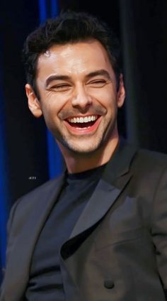 a smiling man in a black suit sitting down