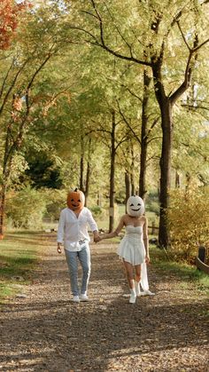 a man and woman walking down a dirt road holding hands in front of some trees