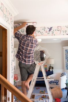 a man standing on a ladder painting the ceiling in his living room with wallpaper