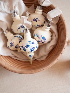 small white vases with blue flowers on them in a wooden bowl next to napkins