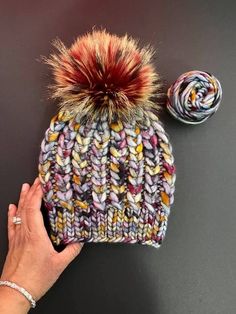 a hand is holding a multicolored knitted beanie with a ball of yarn next to it