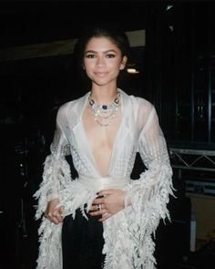 a woman in a white dress with feathers on her arms and chest, posing for the camera