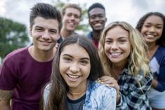 a group of young people standing next to each other smiling at the camera with trees in the background