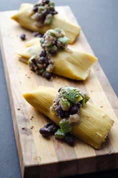 three tamales with black beans and salsa on a wooden cutting board