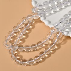 a necklace with clear beads is on a white plate next to a pink wall and a beige background