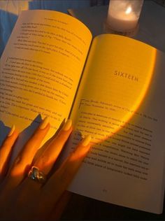 a woman's hand holding an open book in front of her face with bright yellow nails