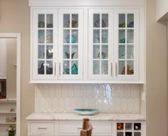 a kitchen with white cabinets and marble counter tops in the center is filled with glassware