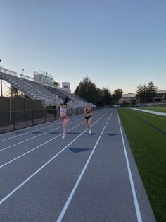 two women running on a race track in front of an empty bleachers at sunset