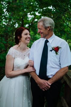 an older man and woman standing next to each other in front of some green trees