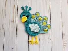 a crocheted peacock sitting on top of a white wooden floor next to a piece of wood