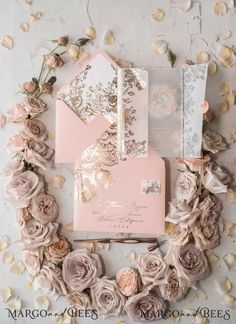 the wedding stationery is surrounded by pink flowers and gold foiled envelopes, which are embellished with roses