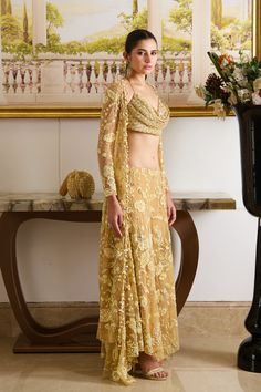 Step into the spotlight with our golden glamour co-ord set, featuring a glamorous cowl-neck top paired up with flowy pants and a complimentary full-sleeved jacket adorned with golden floral embroidery crafted out of precious sequins, crystals, and dainty detailing. The tie-up cowl neck designer blouse features intricate fish scale pattern embroidery with sequins and beads, and the heavily embellished flower motifs adorn the jacket and wide-legged flowy pants. Cowl neck blouse adorned with fish s Gold Floor-length Palazzo Set For Designer Wear, Gold Embroidered Party Sets, Glamorous Floral Embroidered Sets For Reception, Elegant Fitted Palazzo Set With Gold Embroidery, Glamorous Sets With Floral Embroidery For Reception, Elegant Palazzo Set With Gold Embroidery For Reception, Glamorous Gold Sharara For Designer Wear, Gold Floor-length Pre-draped Saree For Evening, Evening Party Wear Palazzo Set With Zari Work