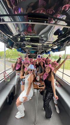 a group of women wearing pink hats on top of a bus with their arms in the air