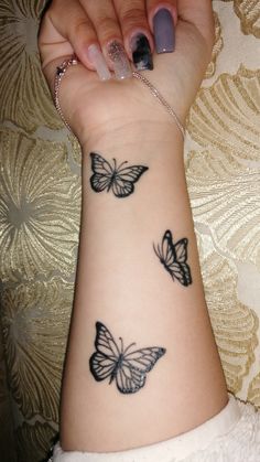 a woman's arm with three butterflies tattooed on the wrist and one is black