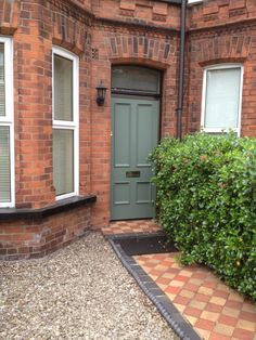 a green door is in front of a brick building with white windows and red bricks