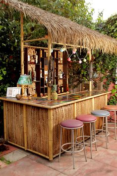 a man standing in front of a bar with stools and a straw roof over it