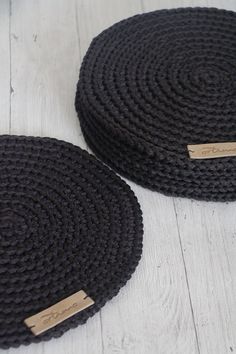 two black braided placemats sitting on top of a white wooden floor