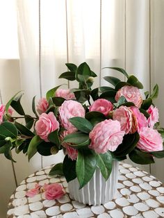 a white vase filled with pink flowers on top of a table