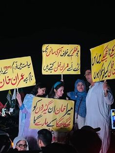 people holding up signs in arabic and english on the side of a road at night