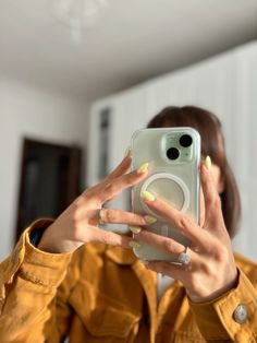 a woman taking a selfie with her cell phone in front of her face and yellow nail polish