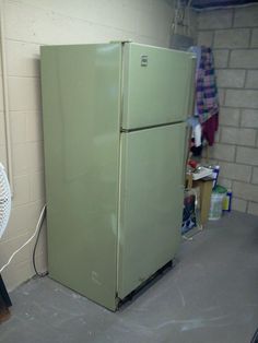 a green refrigerator sitting in the corner of a room next to a fan and other items