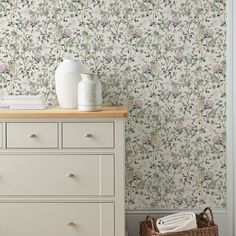 a white dresser sitting next to a wall with flowers on it and a basket in front of it