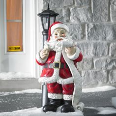 a santa clause figurine is standing in the snow next to a lamp post