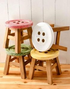 three wooden stools with buttons on them sitting on a wood floor in front of a white wall