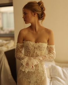 a woman in a wedding dress is standing near a bed and looking off to the side