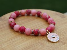 Show your love for OMORI with a handmade bracelet themed around characters from the game! This bracelet inspired by Sweetheart features her signature pink color palette as well as a doughnut charm. This would make a great gift for any fan of the game! The bracelet is made from 8mm genuine rhodochrosite and sea sediment jasper with an enamel doughnut charm. It is strung on elastic cord sized to fit a 6in wrist but will stretch to fit a larger wrist. If you need a custom size, feel free to reach o Pink Charm Bracelet With Round Beads For Friendship, Pink Round Beads Charm Bracelet For Friendship, Pink Round Bead Bracelets For Birthday Gift, Pink Round Beads Bracelet For Birthday, Pink Playful Bracelets For Birthday Gift, Pink Round Beads Bracelets For Birthday Gift, Pink Beaded Bracelets For Birthday, Pink Stretch Bracelet For Valentine's Day Gift, Trendy Pink Beaded Bracelets For Birthday Gift