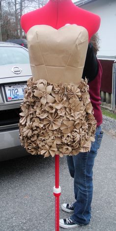 a woman standing next to a mannequin wearing a dress made out of paper