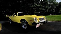 a yellow car parked on the side of a road next to a lush green field