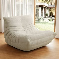 a white bean bag chair sitting on top of a hard wood floor next to a window