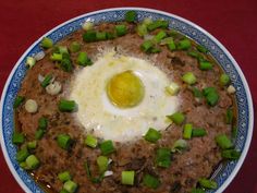 an egg is on top of some food in a blue and white bowl with green onions