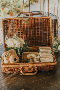 a wicker suitcase filled with books and other items sitting on a table next to a vase