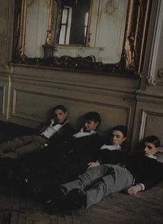 four young men laying on the floor in front of a large mirror and gold framed painting