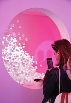 a woman is looking at her cell phone in front of a pink wall with bubbles