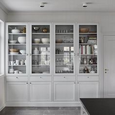 a kitchen with white cabinets and black counter tops in front of a large glass doored cabinet