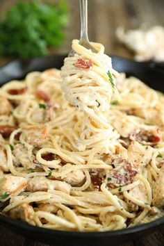 a fork full of pasta with chicken and parmesan cheese on it in a skillet