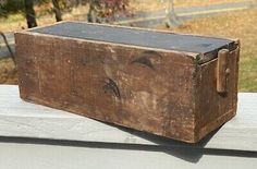 an old wooden box sitting on top of a table next to some grass and trees