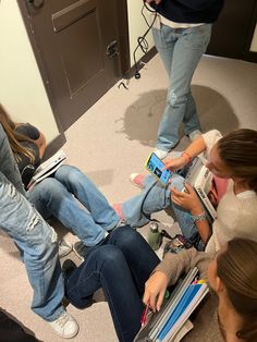 several people sitting on the floor with cell phones in their hands and one person holding a book