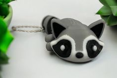 a raccoon shaped keychain sitting on top of a table next to plants