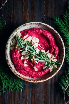 beet hummus with almonds and herbs in a bowl on a wooden table