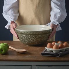 a woman holding a bowl with eggs in it on a wooden table next to other bowls and utensils