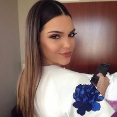 a woman holding a cell phone in her right hand and wearing a white top with blue flowers on it