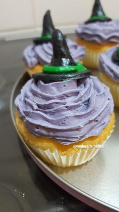 three cupcakes with purple frosting and witches hats on top are sitting on a silver plate