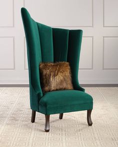 a green velvet chair with a fur pillow on it's back and legs, in front of a white paneled wall