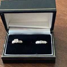 two silver rings in a black box on a wooden table with the lid open to show it's inside