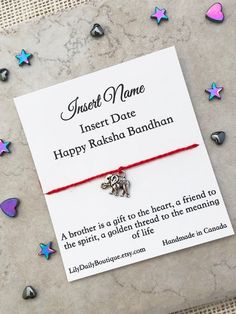 a red string bracelet with silver bells and hearts on it, sitting next to a card that says insert name