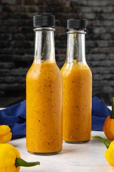 two glass bottles filled with mustard sitting on top of a table next to yellow peppers